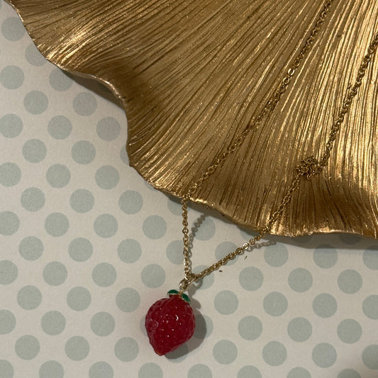 Necklace with a strawberry pendant on a gold leaf and polka dot background