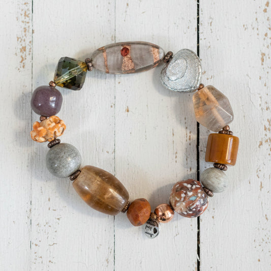 A beaded stretch bracelet made of various natural stones and beads in earthy brown, gray, white, and orange tones,