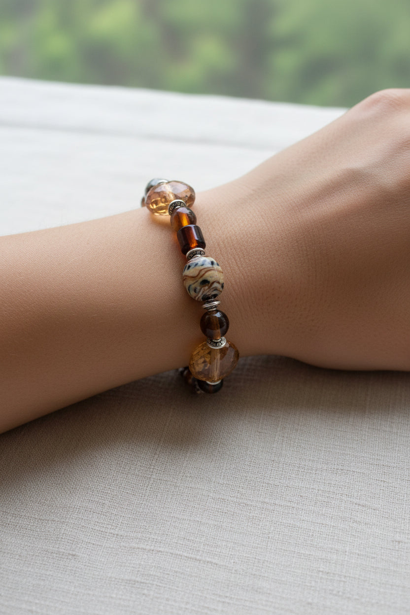 A beaded stretch bracelet featuring brown and amber glass beads, a marbled brown bead, and clear faceted beads.