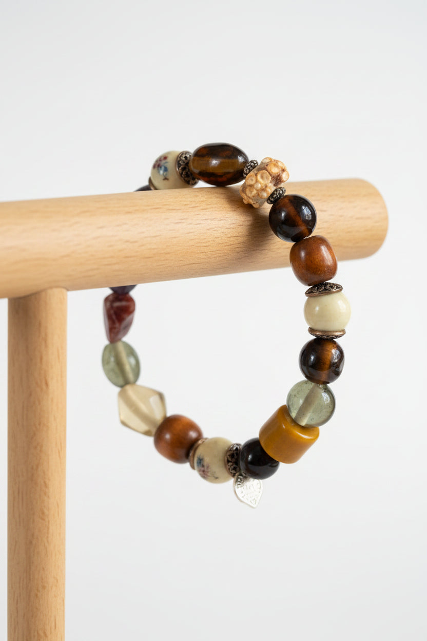 A beaded stretch bracelet featuring a mix of polished and textured stone beads in brown, orange, white, and black, with a small silver metal charm, displayed on display.