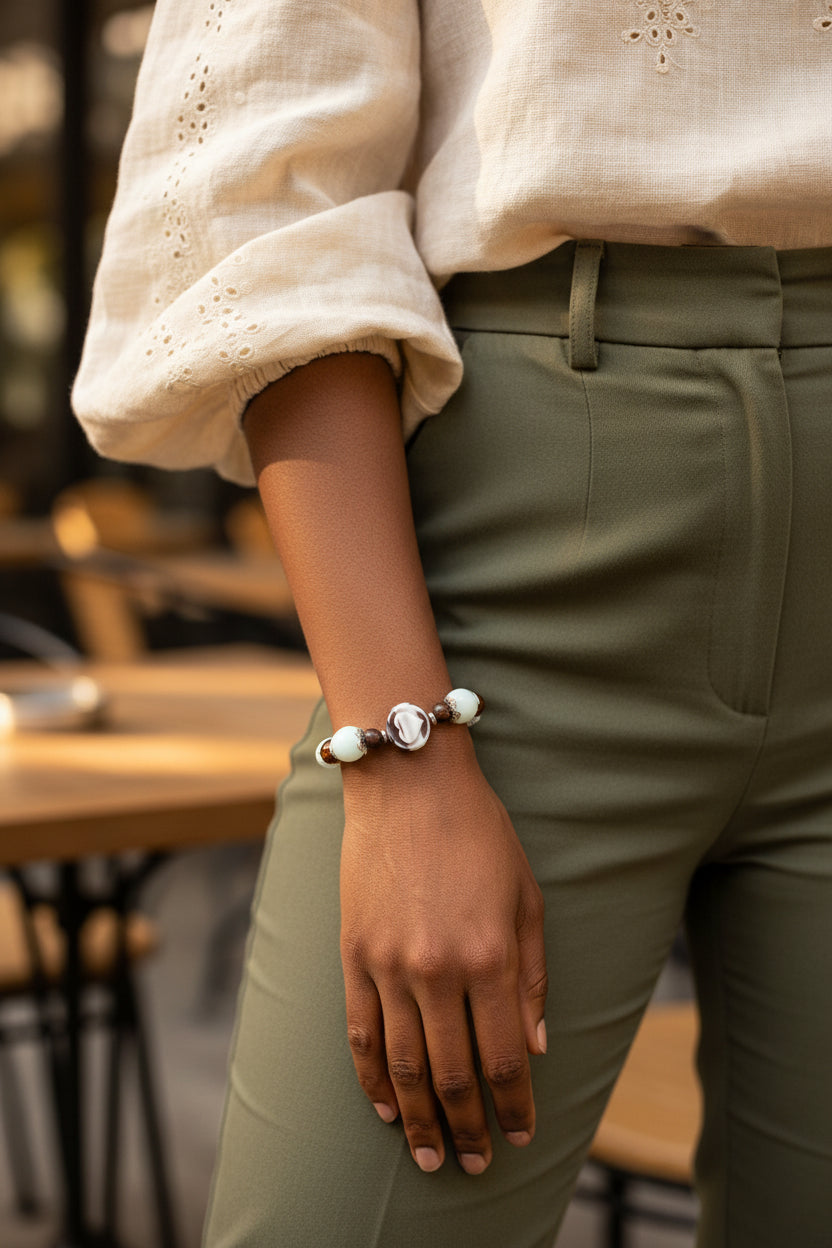A beaded stretch bracelet featuring light blue-green turquoise beads, dark brown translucent beads, a central white and black marbled oval charm, and silver-toned spacer beads, displayed on a woman's arm