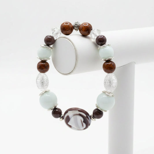 A beaded stretch bracelet featuring light blue-green turquoise beads, dark brown translucent beads, a central white and black marbled oval charm, and silver-toned spacer beads, displayed on a stand