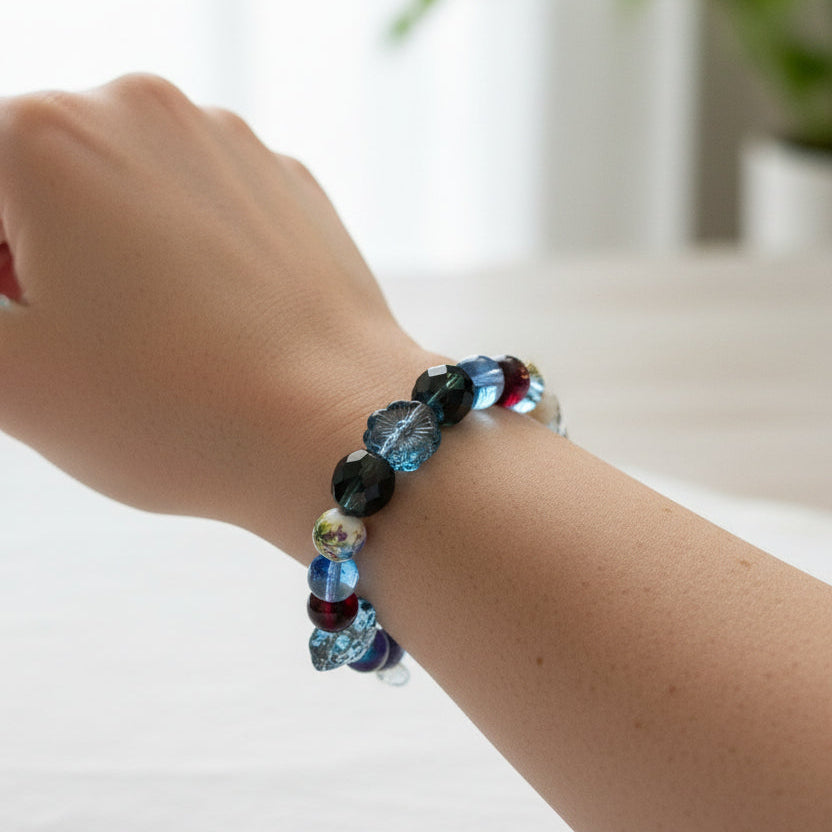 A beaded stretch bracelet featuring a mix of blue, black, and dark red beads, including faceted round beads, a white bead with yellow details, and a dark gray stone accent,