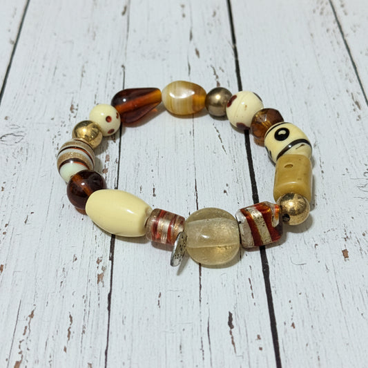 A handmade beaded stretch bracelet featuring a variety of beads in cream, brown, amber, and striped patterns, displayed on a white background.