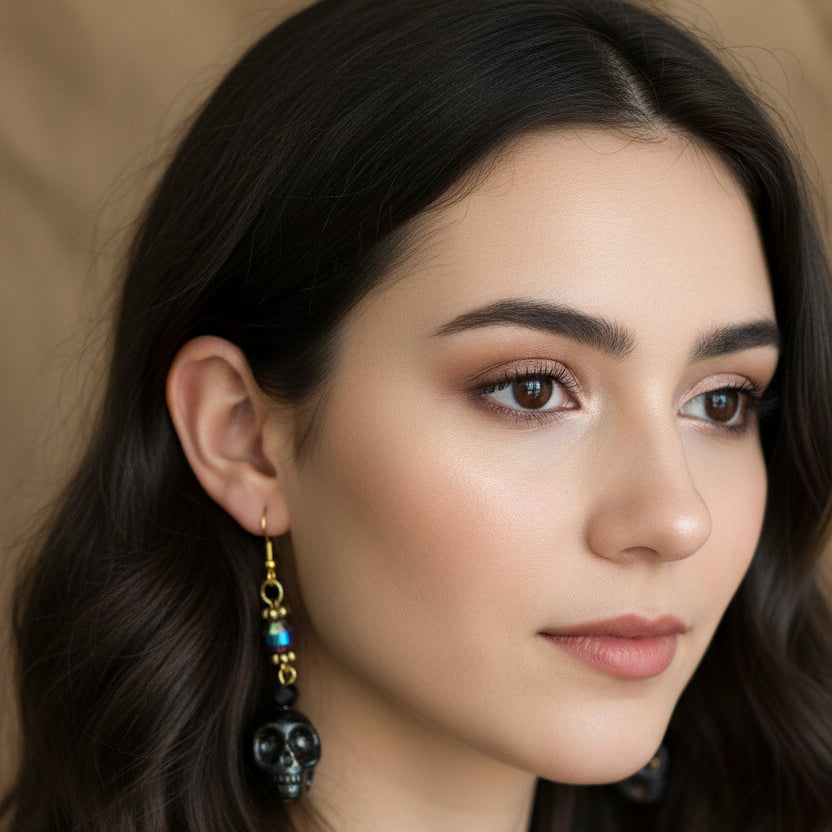 A pair of handmade dangle earrings featuring black marbled skull charms, iridescent beads, and gold hooks, displayed on young woman