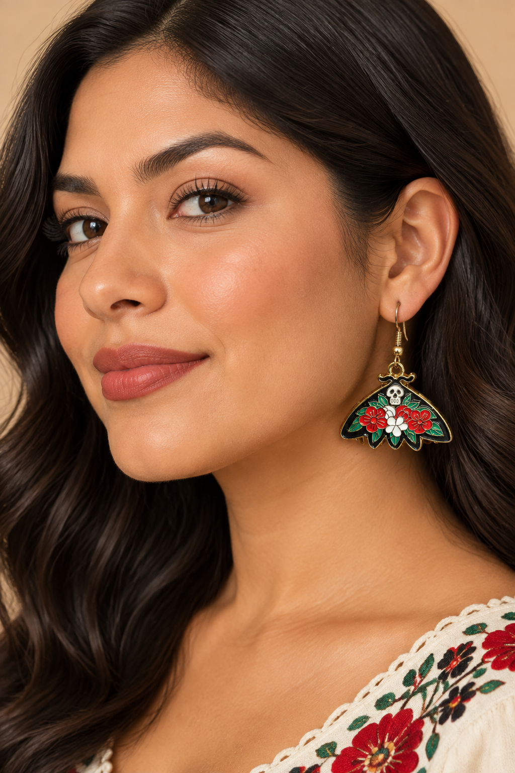 A pair of gothic butterfly drop earrings featuring red and white flowers, green leaves, skull details, and gold-tone hooks on a lady. 