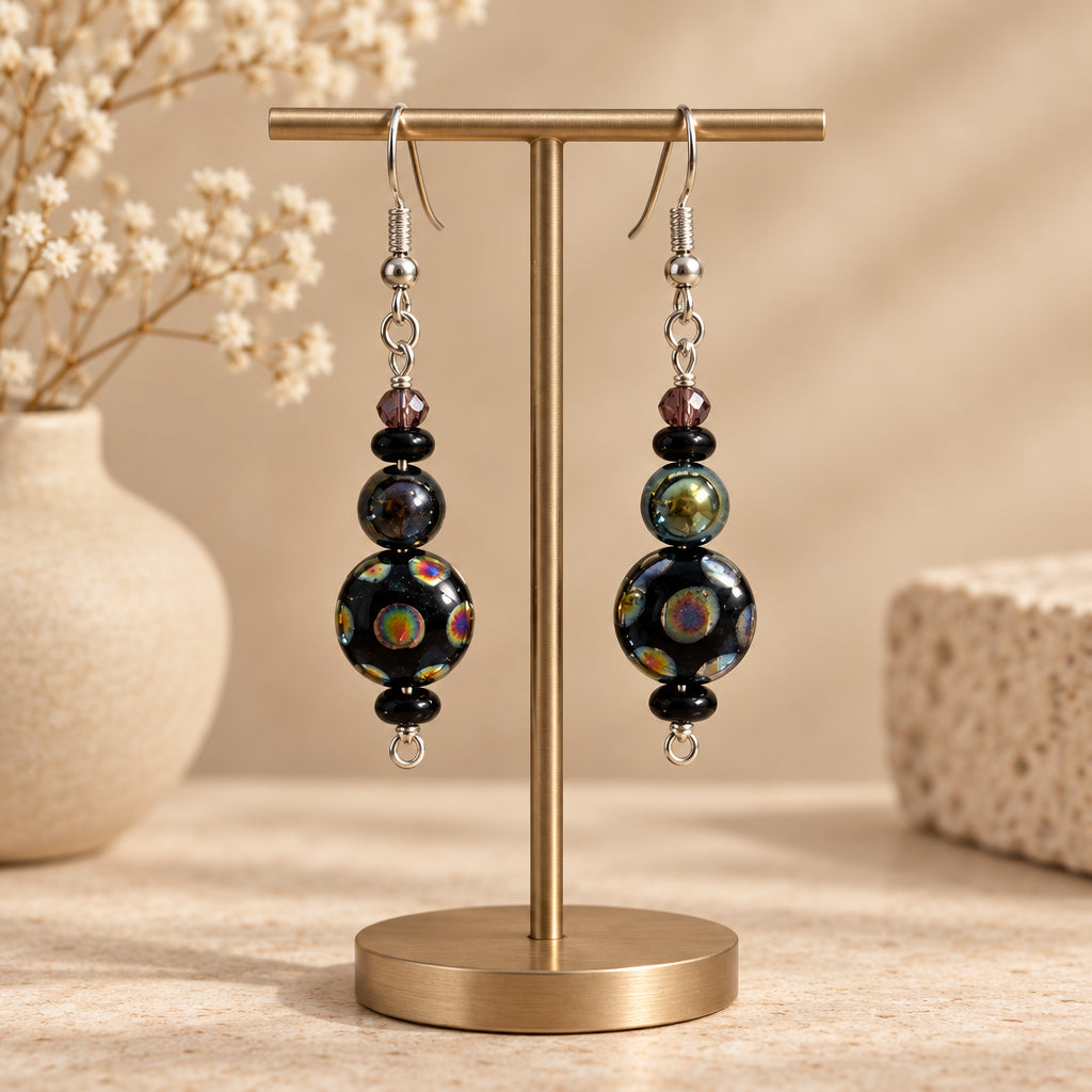 A pair of handmade dangle earrings with black iridescent beads, small dark beads, and silver fishhook wires, displayed on a earring stand 