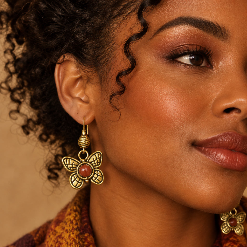 A pair of gold-tone butterfly dangle earrings with textured wings and round reddish-brown stone centers, displayed on a woman.