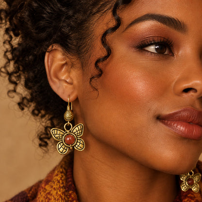 A pair of gold-tone butterfly dangle earrings with textured wings and round reddish-brown stone centers, displayed on a woman.