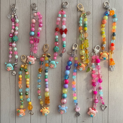 A collection of colorful beaded phone strap keychains with charms, laid out on a light-colored wooden surface.