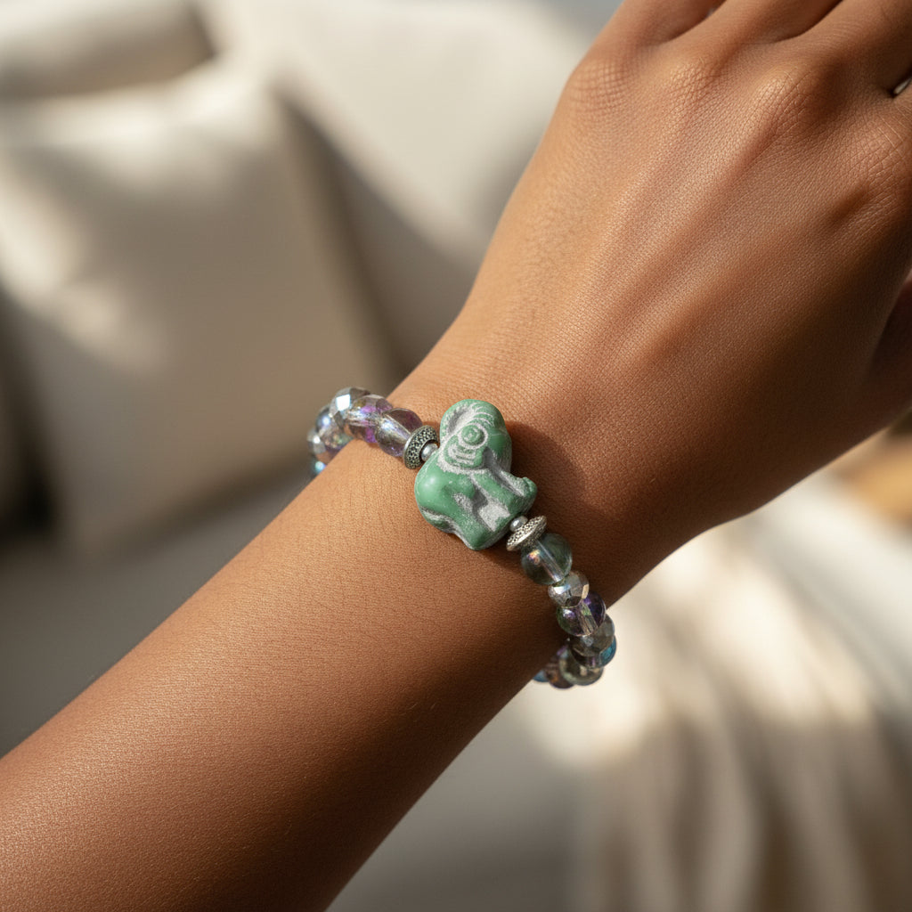 A beaded stretch bracelet featuring faceted iridescent beads, silver-toned spacer rings, and a central carved green elephant charm, displayed on a woman's arm