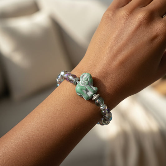 A beaded stretch bracelet featuring faceted iridescent beads, silver-toned spacer rings, and a central carved green elephant charm, displayed on a woman's arm