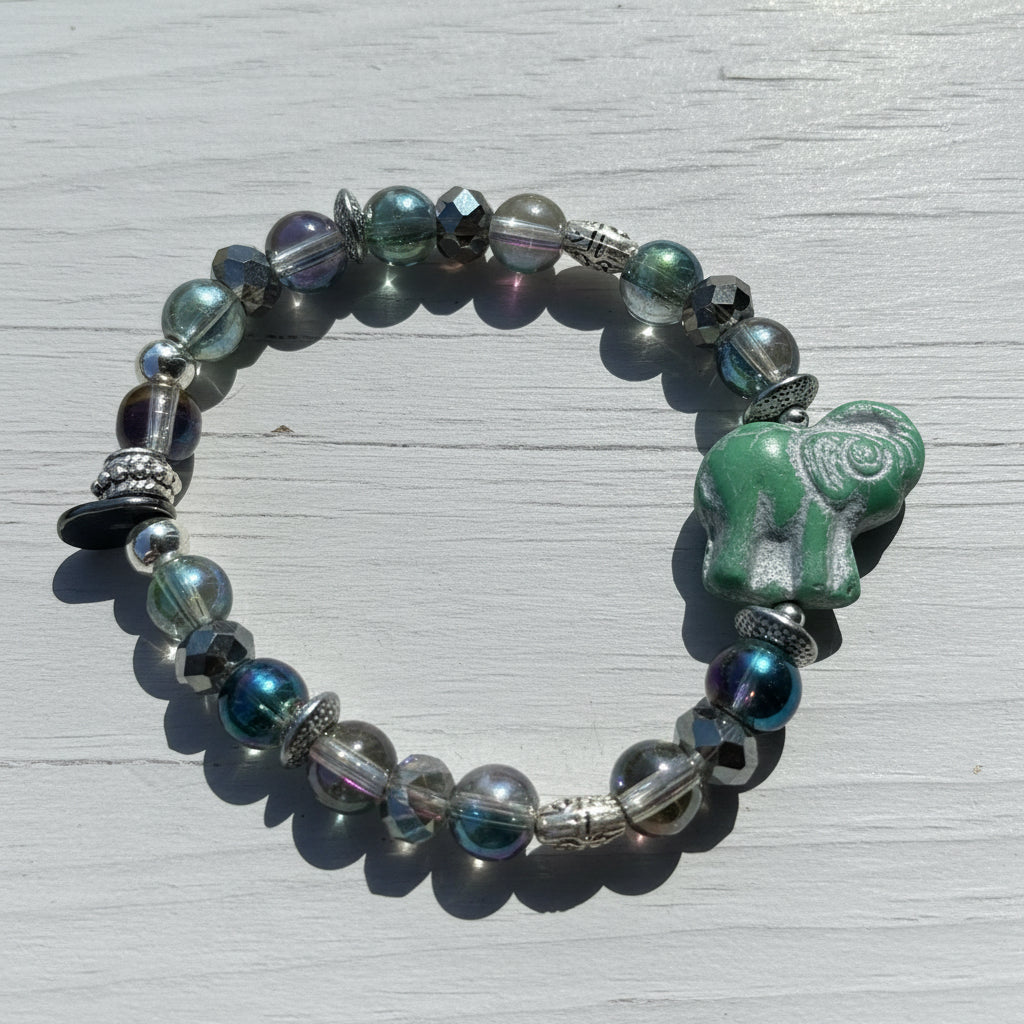 A beaded bracelet with faceted iridescent beads, silver-toned spacers, and a green elephant-shaped bead, displayed on a weathered wooden surface.