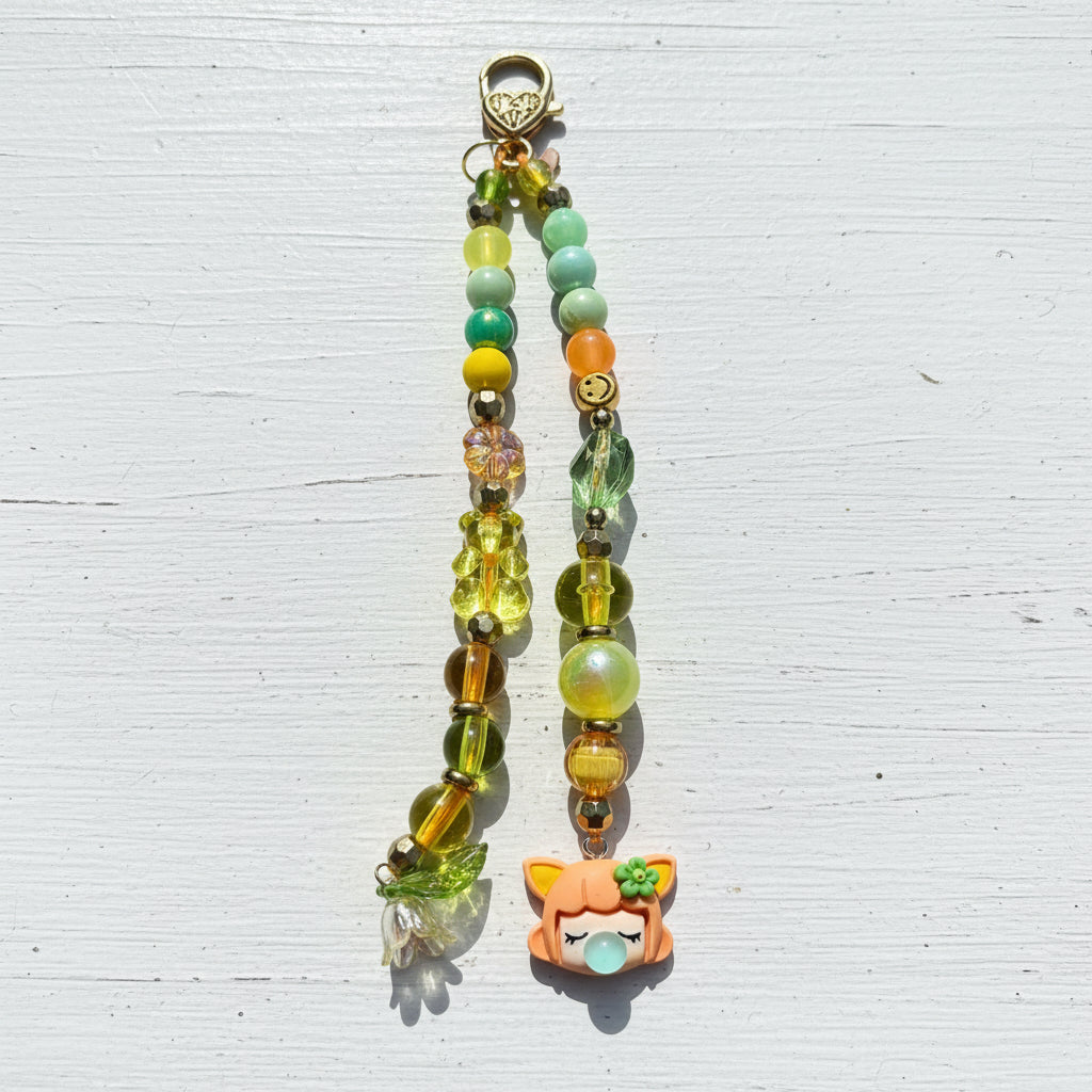A colorful beaded charm strap with a small orange cartoon fox charm, displayed on a weathered gray wooden surface.