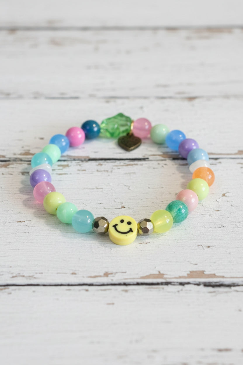 A colorful beaded bracelet with pastel round beads, a green faceted bead, a small gold heart charm, and a yellow smiley face charm