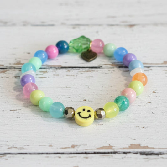 A colorful beaded bracelet with pastel round beads, a green faceted bead, a small gold heart charm, and a yellow smiley face charm
