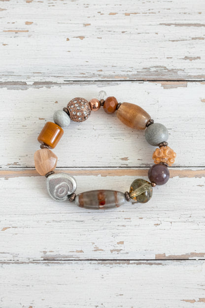 A beaded stretch bracelet with a mix of earthy, metallic, and stone-like beads in brown, orange, silver, and green.
