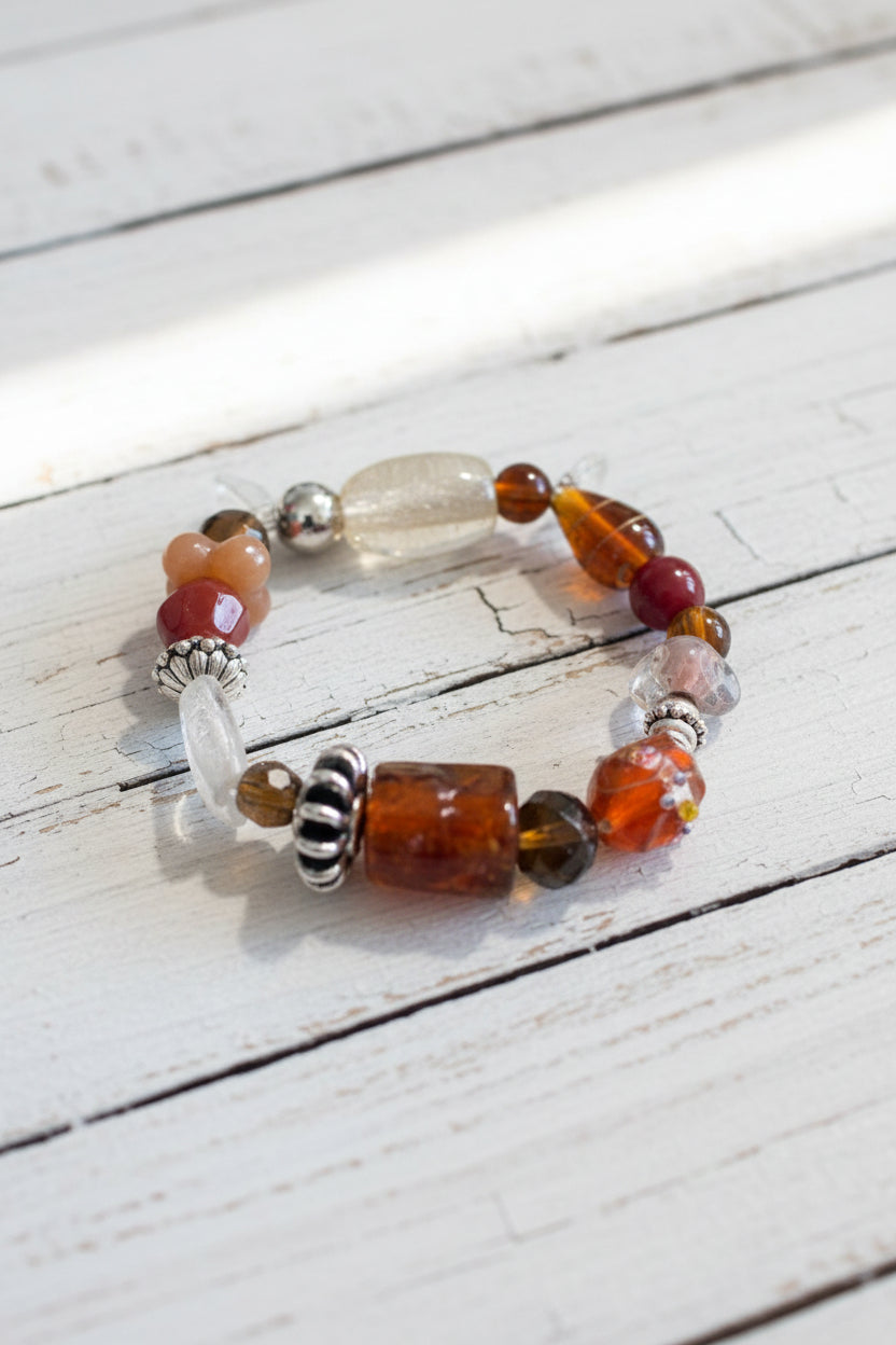 A beaded stretch bracelet featuring a large central brown cylindrical bead, a clear faceted bead, and smaller red, orange, and silver beads.