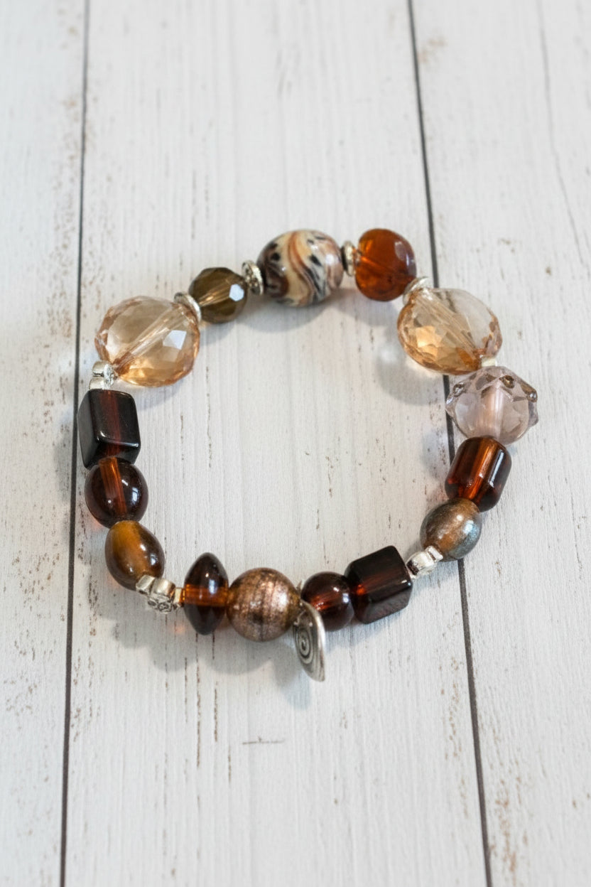 A beaded stretch bracelet featuring a mix of brown, amber, clear, and metallic beads, displayed on a white background.