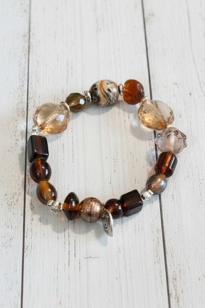 A beaded stretch bracelet featuring a mix of brown, amber, clear, and metallic beads, displayed on a white background.
