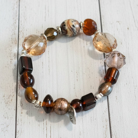 A beaded stretch bracelet featuring a mix of brown, amber, clear, and metallic beads, displayed on a white background.