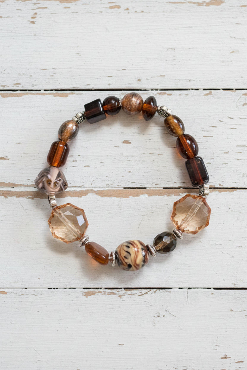 A beaded stretch bracelet featuring brown, black, and clear faceted beads with a central patterned brown bead, displayed on a white background.