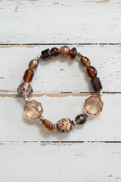 A beaded stretch bracelet featuring brown, black, and clear faceted beads with a central patterned brown bead, displayed on a white background.