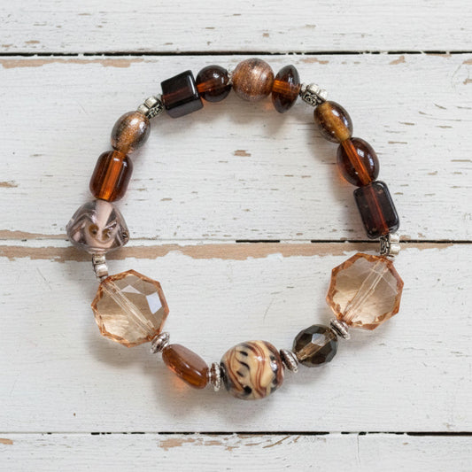 A beaded stretch bracelet featuring brown, black, and clear faceted beads with a central patterned brown bead, displayed on a white background.