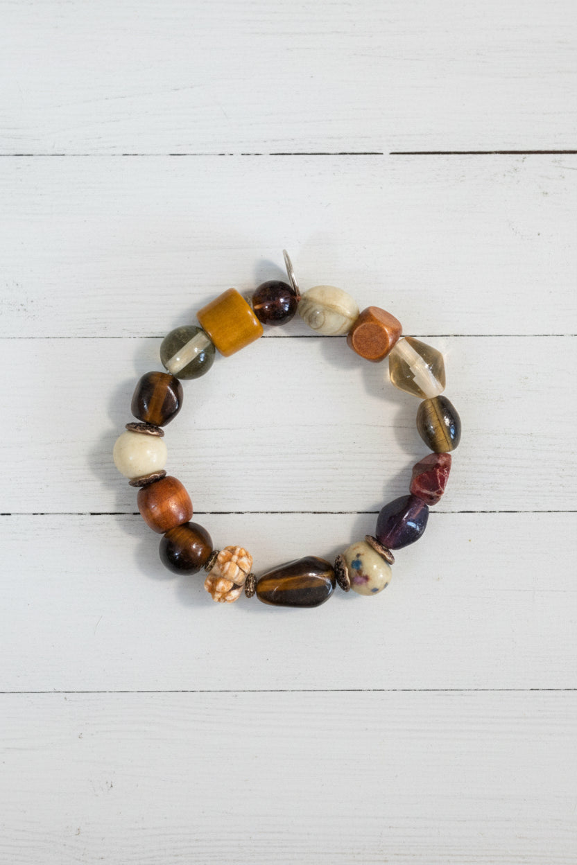 A beaded stretch bracelet featuring a mix of polished and textured stone beads in brown, white, orange, and black, displayed on a white background.
