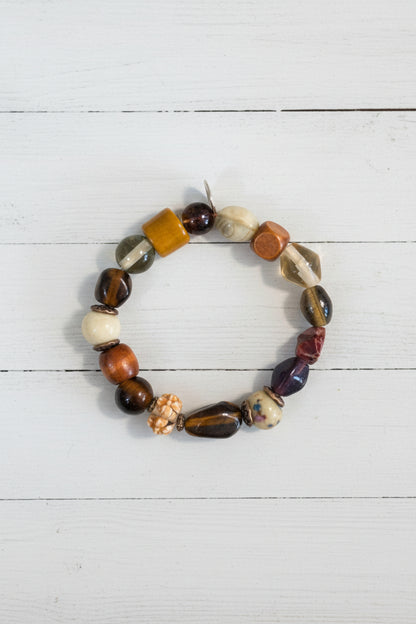 A beaded stretch bracelet featuring a mix of polished and textured stone beads in brown, white, orange, and black, displayed on a white background.