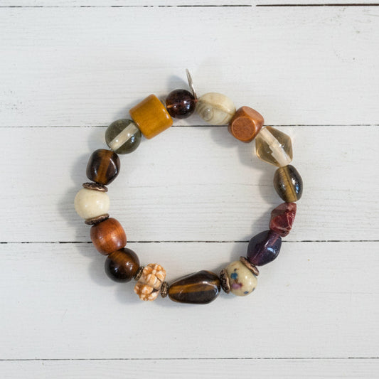 A beaded stretch bracelet featuring a mix of polished and textured stone beads in brown, white, orange, and black, displayed on a white background.