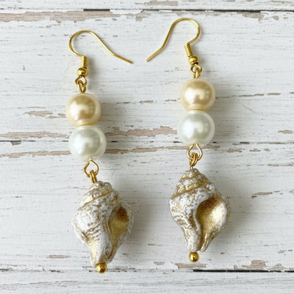 A pair of dangling earrings with gold-tone hooks, three pale pearls, and textured shell charms in silver and gold, displayed on a white background.