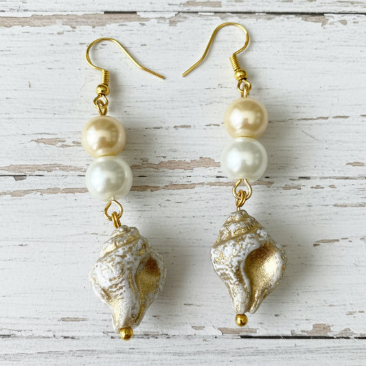A pair of dangling earrings with gold-tone hooks, three pale pearls, and textured shell charms in silver and gold, displayed on a white background.