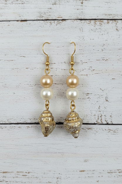 A pair of gold and pearl drop earrings with textured gold charms, displayed on a white ceramic stand against a white background.