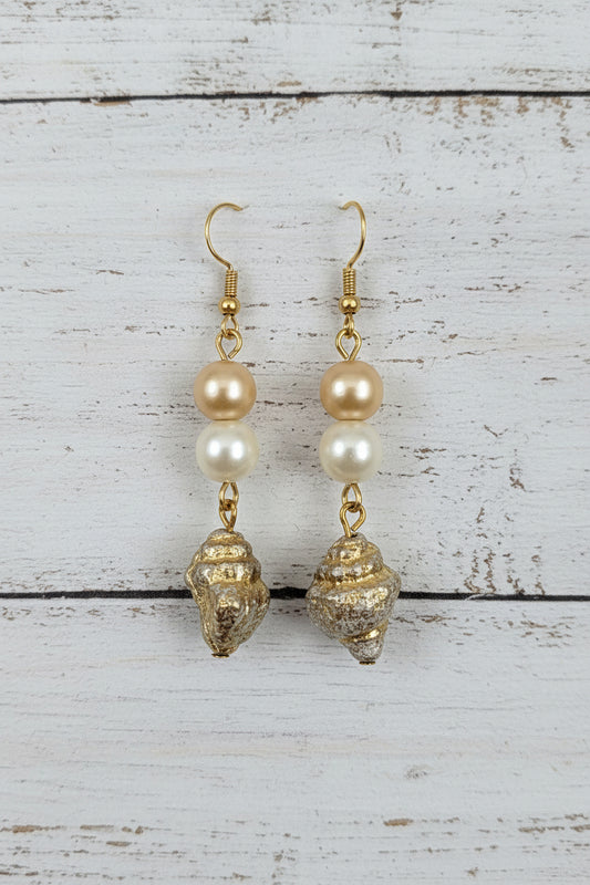 A pair of gold and pearl drop earrings with textured gold charms, displayed on a white ceramic stand against a white background.