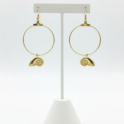 A pair of gold hoop earrings with textured shell charms, displayed on a earring stand