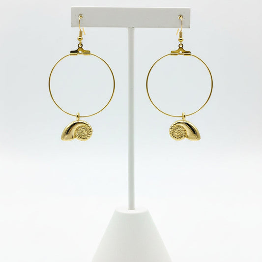 A pair of gold hoop earrings with textured shell charms, displayed on a earring stand