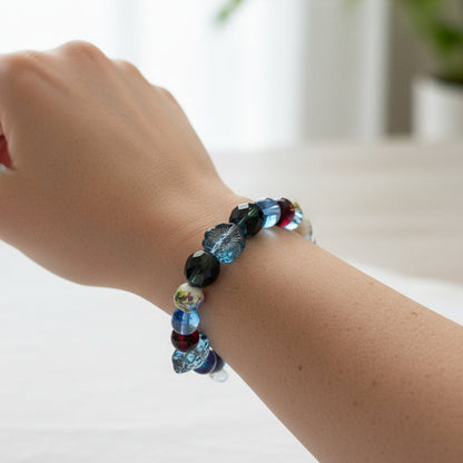 A beaded stretch bracelet featuring a mix of blue, black, and dark red beads, including faceted round beads, a white bead with yellow details, and a dark gray stone accent,