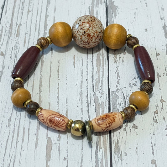 A beaded stretch bracelet featuring natural wood beads, a brown agate stone, and dark reddish-brown cylindrical beads, displayed on a textured white surface.