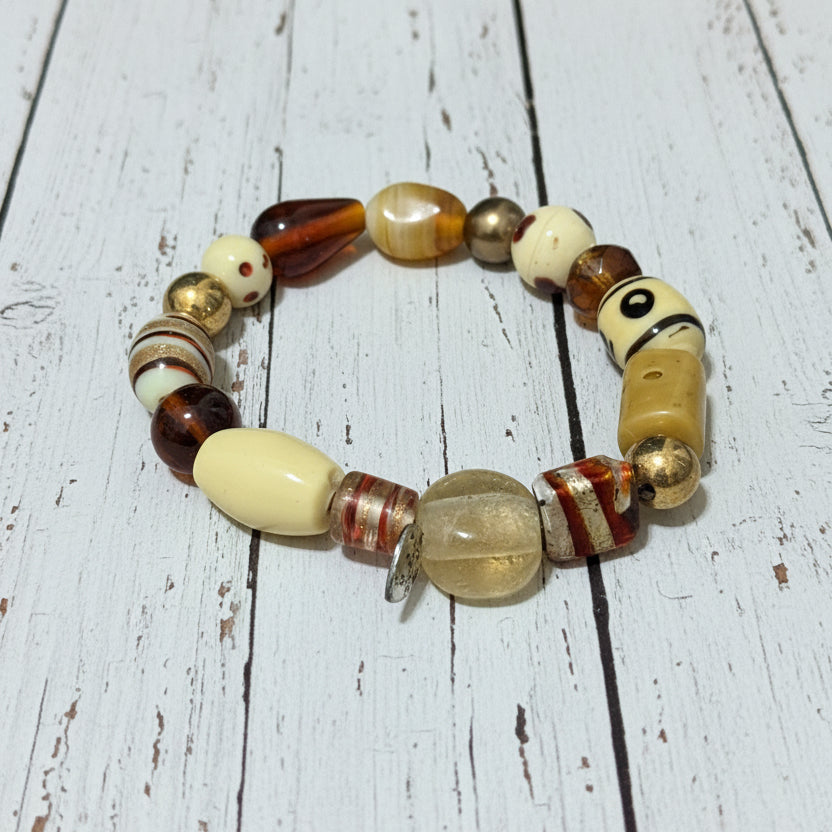 A handmade beaded stretch bracelet featuring a variety of beads in cream, brown, amber, and striped patterns, displayed on a white background.