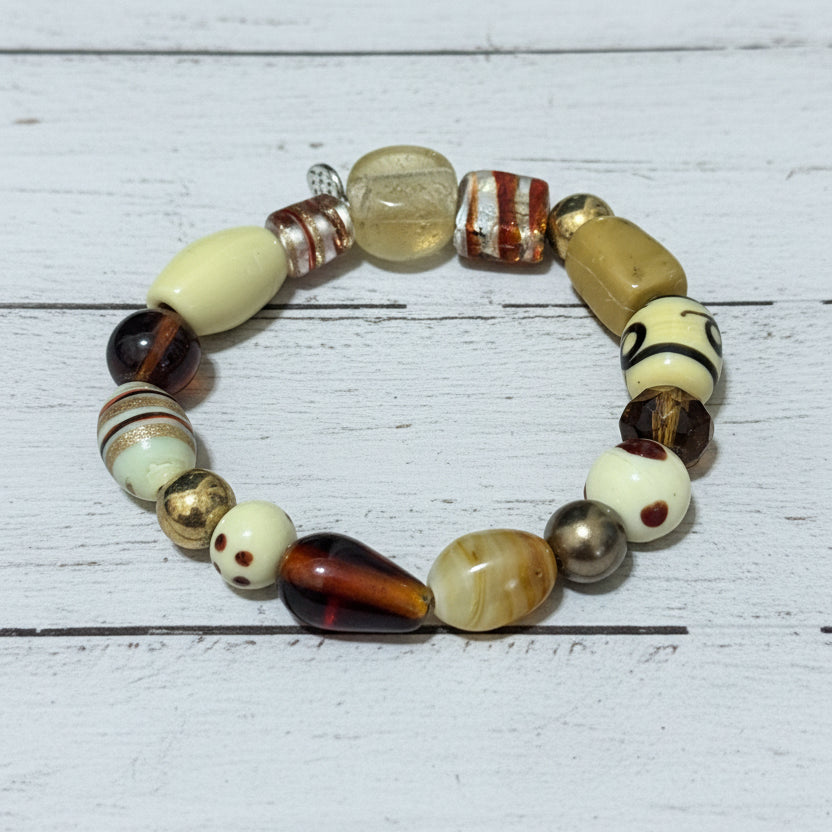A beaded stretch bracelet featuring a variety of textured, patterned, and glossy beads in cream, brown, black, and metallic gold, displayed on a white background.