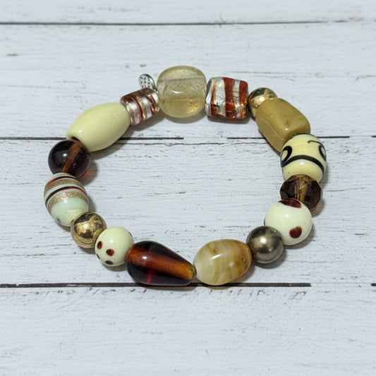 A beaded stretch bracelet featuring a variety of textured, patterned, and glossy beads in cream, brown, black, and metallic gold, displayed on a white background.