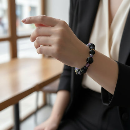 A beaded stretch bracelet featuring glossy black faceted beads, textured black striped beads, polished black beads, and small purple and metallic gold accent beads, displayed on a woman's arm.